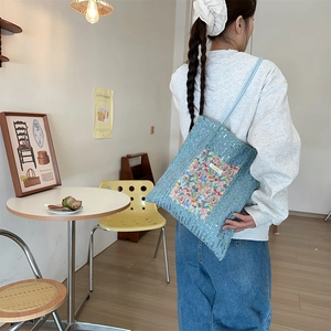 Detailed shot of light blue sequined canvas tote bag with floral patch pocket and twin straps