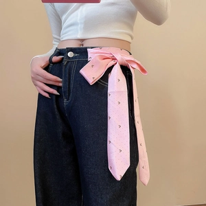 Pink polka dot silk bow accessory tied on dark blue denim jeans for a stylish waist accent