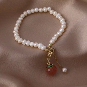 Detail of freshwater pearl bracelet with golden clasp and red persimmon pendant