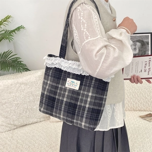 Close-up of black plaid tote bag with white lace trim and Happy patch on a white sofa