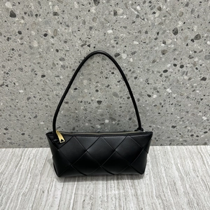 Macro detail of black woven leather handbag with gold zipper on a wooden desk