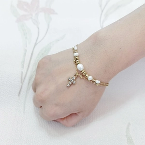 Close-up of double-layer pearl bracelet with a gold cross pendant and clear crystals