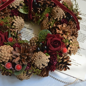 Christmas wreath with pine cones, red roses, and berries featuring a red velvet ribbon