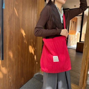 Detail of red quilted tote bag featuring a brand patch and long shoulder strap