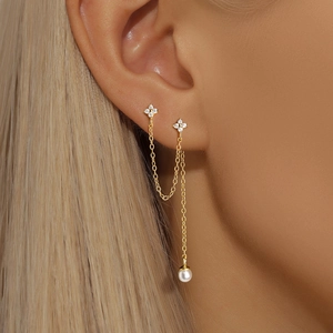 Close-up of gold double ear piercing earrings with zircon flowers and pearl drop