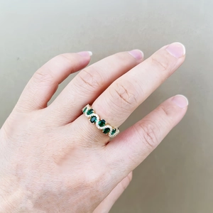 Close-up of a gold ring featuring an oval emerald and small zircon accents on a finger