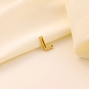 Vue macro d'un pendentif lettre L dorée sur tissu beige pour bijoux personnalisés
