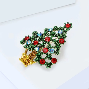 Golden Christmas tree brooch with green enamel and colorful rhinestones on a white pedestal