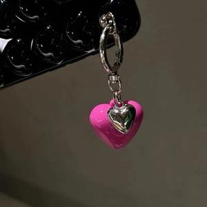 Close-up of a pink heart-shaped charm with a silver ring and a small metal pendant