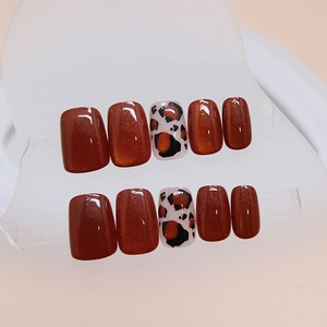 Cat eye and leopard print press-on nails in reddish amber tones displayed on a clear stand