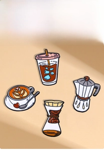 Detail of coffee enamel pins featuring latte art cup and mocha pot on beige background
