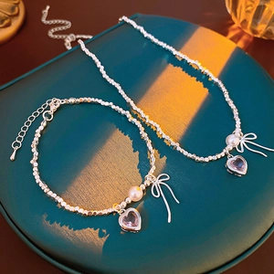 Detailed view of silver beaded necklace and bracelet with pink heart and bow charms
