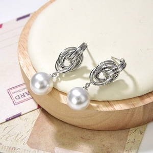 Elegante silberne Knot Ohrringe mit weißen Perlen auf antikem Holzständer