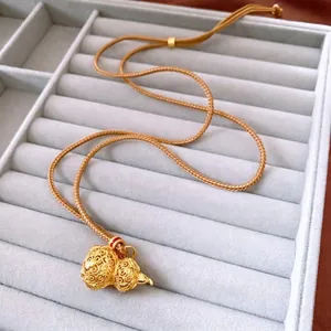 24k gold-plated hollow Wu Lou pendant necklace with brown braided rope on jewelry tray