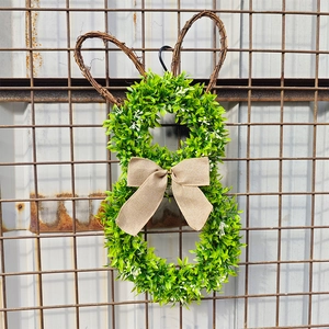 Easter rabbit wreath with green leaves, rattan ears and burlap bow on a metal mesh