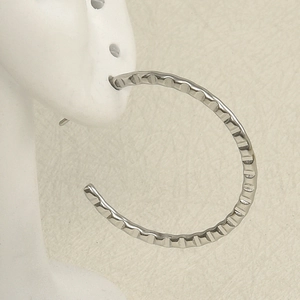 Macro detail of silver C-shape hoop earrings with wavy texture on a model ear