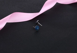 Detailed view of silver crystal stud earrings in blue-green finish on black silk background