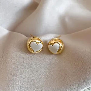 Minimalist golden dome stud earrings with white heart inlay on soft silk background