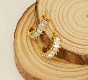 Detail of gold U-shaped hoop earrings with rectangular crystals on a wooden base