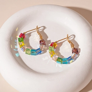 Detail of colorful geometric glass cube beads on golden hoop earrings with rainbow light