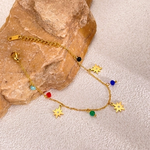 Detail of gold stainless steel bracelet with colorful beads and star charms on stone