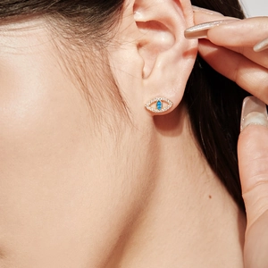 Gros plan sur une boucle d'oreille Evil Eye dorée avec pierre bleue et zircons
