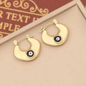 Detail of gold evil eye hoop earrings with black enamel on a beige jewelry tray