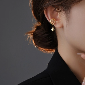 Close-up of golden multi-layer heart charm ear cuff on ear with a minimalist backdrop
