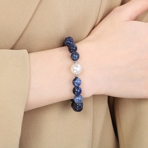 Close-up of blue lapis beads and a white pearl bracelet with an OT clasp on a model