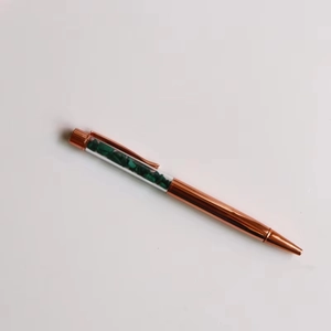 Detail view of rose gold ballpoint pen with green crystal gravel stones in transparent top