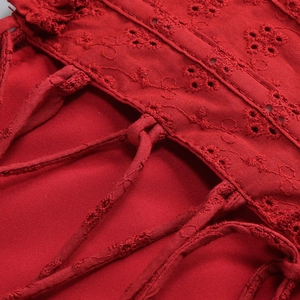 Macro detail of red off-shoulder dress featuring eyelet embroidery and lace-up design