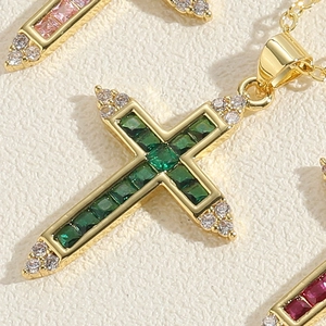 Macro shot of 14K gold plated cross pendant with emerald green zircons and tiny diamonds