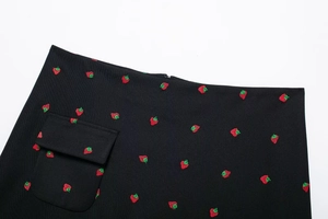 Détail de la jupe noire avec broderie de fraises rouges, fermeture éclair et poche à rabat