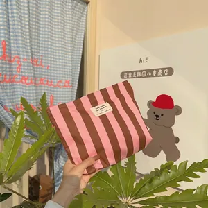 Detail of hand-held pink and brown striped canvas makeup bag with a minimalist white label