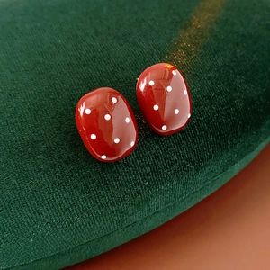Dettaglio di orecchini ovali rossi a pois bianchi su cuscino di velluto verde