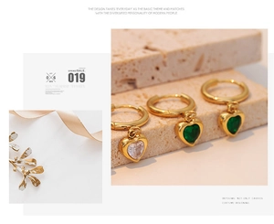 Close-up of golden heart-shaped earrings with emerald and clear zircon inlay