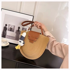 Detail of semi-circular woven cotton bag with brown leather handles and a cute duck charm