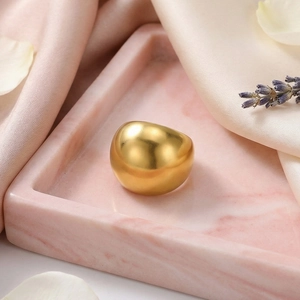 Detailed view of heavy gold round ring on pink marble tray with lavender and petals