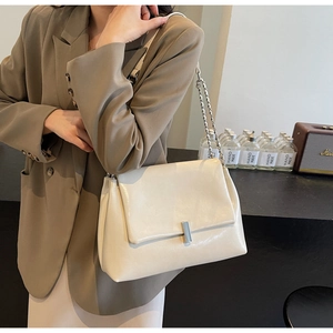Detail of a beige PU leather chain bag with a silver square lock on a stylish model