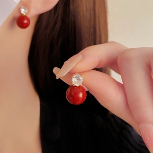Détail de boucles d'oreilles dorées avec perles rouges et oxydes de zirconium brillants