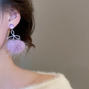 Dettaglio di orecchini a pompon viola con fiocco indossati da una modella per l'inverno