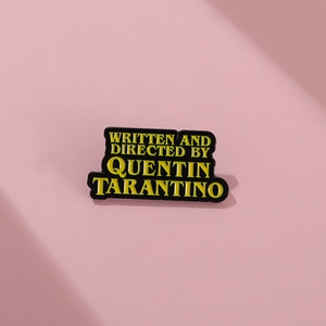 Quentin Tarantino enamel pin with yellow text on black metal over pink background