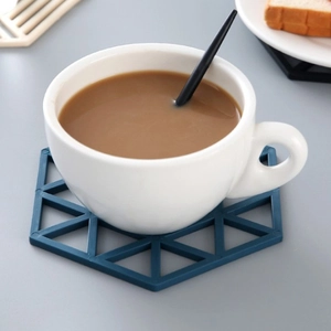 Sous-verre bleu géométrique ajouré avec une tasse à café blanche sur surface grise