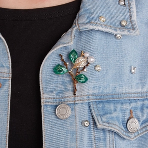 Detailed botanical brooch with green enamel leaves and pearls on denim jacket