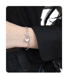 Close-up of silver heart pendant bracelet with OT toggle clasp on model's wrist