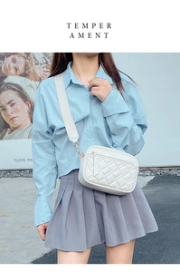 Close-up of white quilted camera bag featuring wide woven strap and gold hardware accents