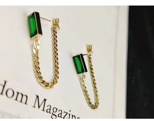 Detail of gold chain earrings featuring emerald-cut green gemstones and U-shaped fringe