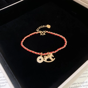 Red woven bracelet with gold horse and coin charms in a velvet gift box on book pages