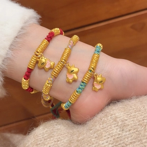 Close-up of woven red and rainbow bracelets with gold charms and cute elephant pendants