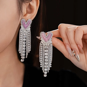 Close-up of elegant long tassel heart earrings with pink rhinestones on a female model